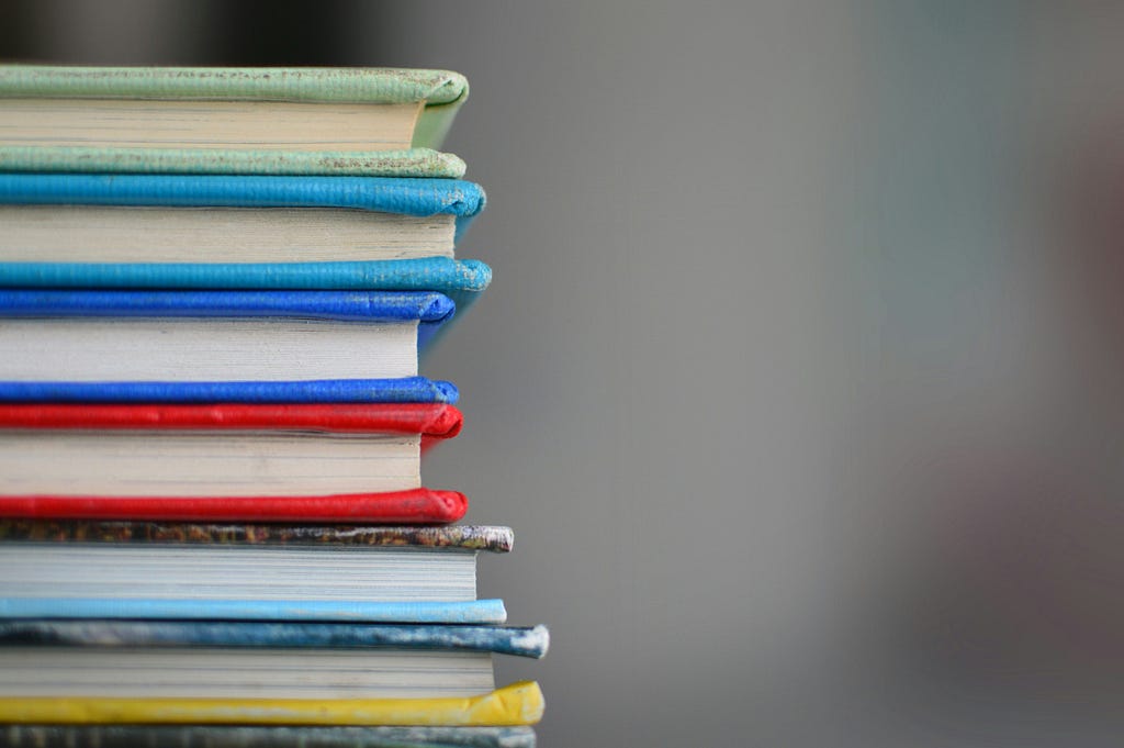 Close-up of a stack of colorful books with frayed edges, arranged in a neat pile against a neutral background.