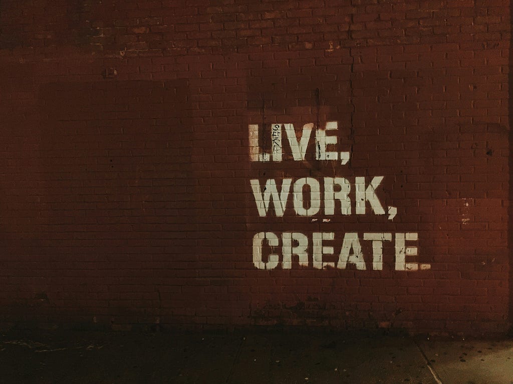 Graffiti on a brick wall with the words ‘LIVE, WORK, CREATE’ stencilled in white paint.